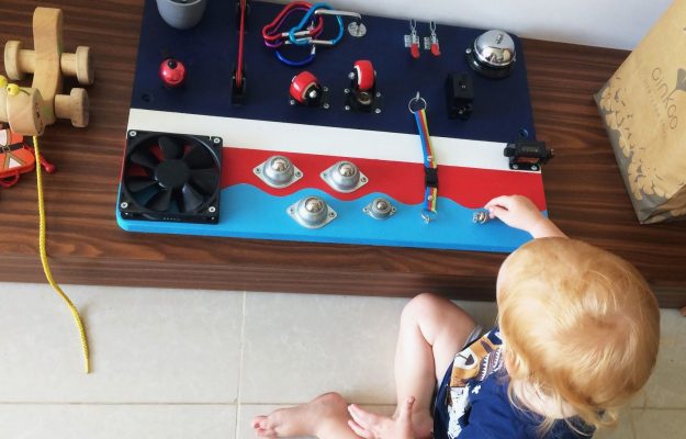 busyboard for two-year-old toddler with the bell, locks, latches and cool design. Little boy playing with activity board.